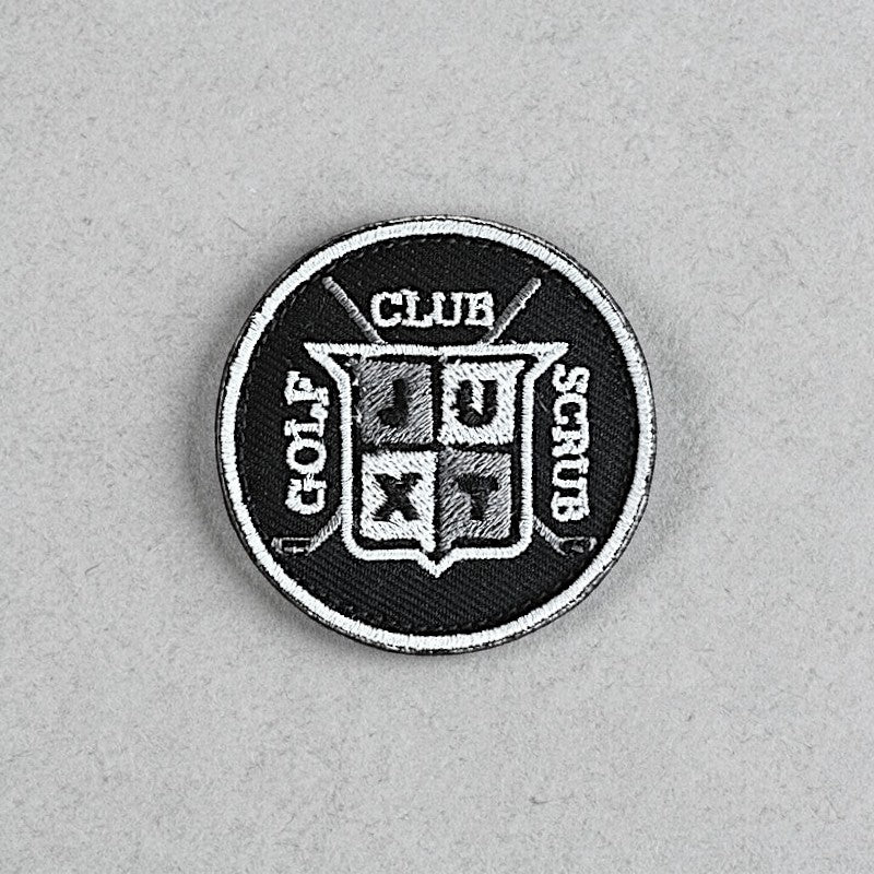 JUXT Golf Co. black circular patch with white and grey embroidery. Features crossed golf clubs and a shield with 'JU' and 'XT' inside.