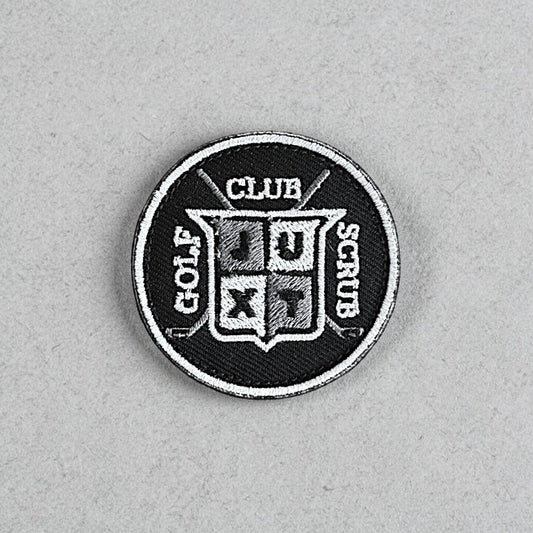 JUXT Golf Co. black circular patch with white and grey embroidery. Features crossed golf clubs and a shield with 'JU' and 'XT' inside.